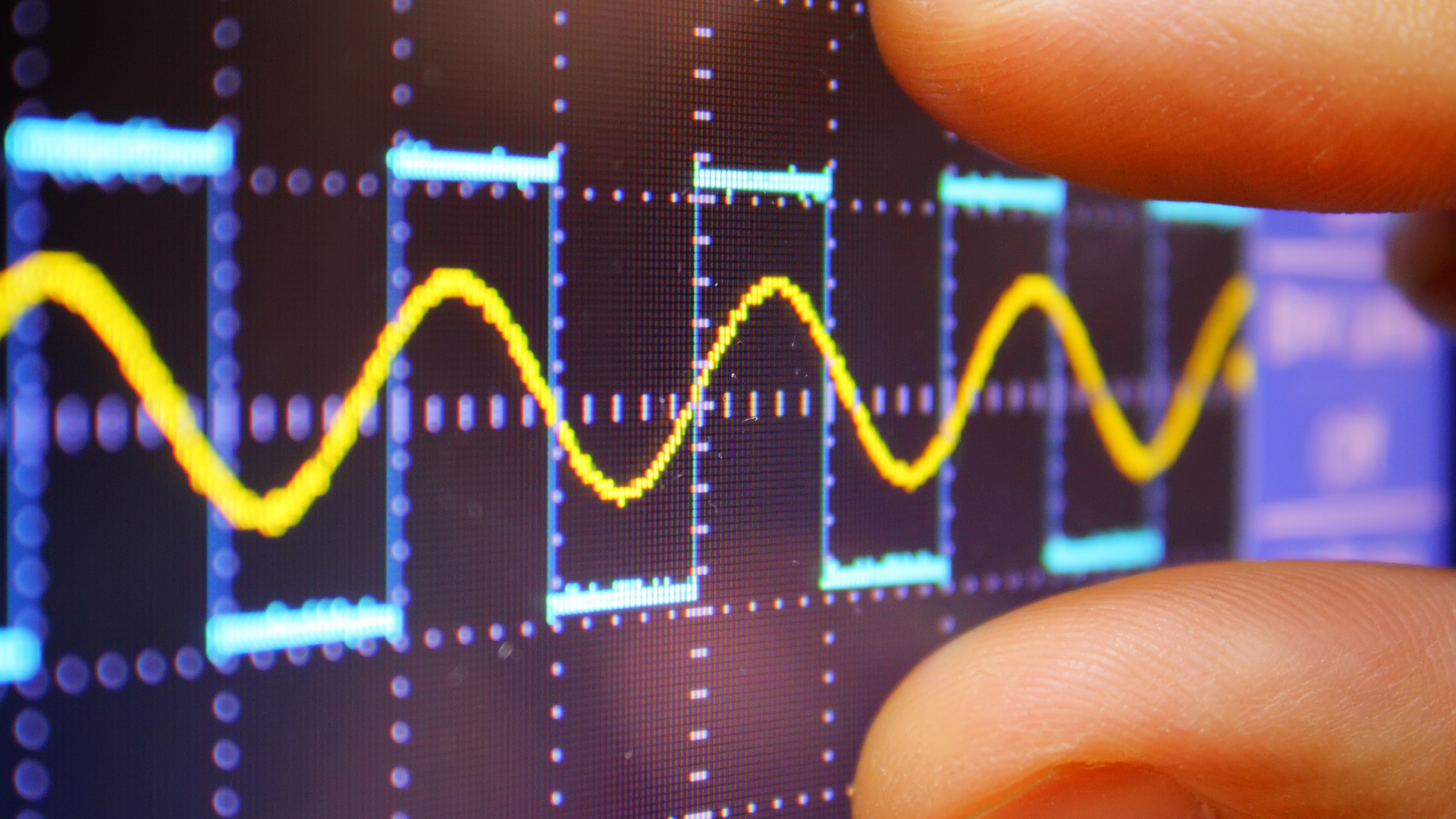 Closeup of two fingers measuring a yellow frequency line on a LCD screen