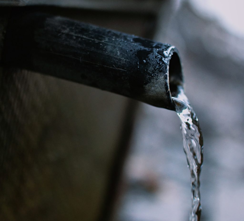 Closeup of clean water flowing out of dark pipe on the side of a bulding