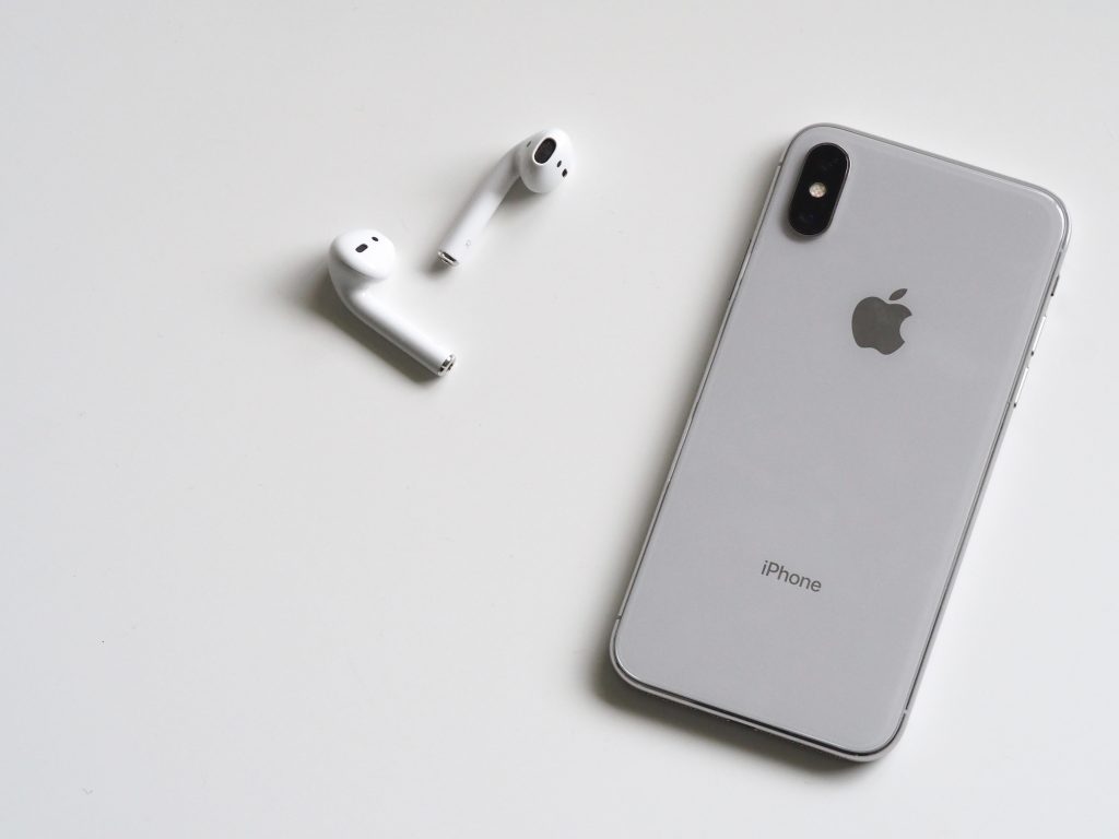 White table with a silver Iphone facedown next to white airpods