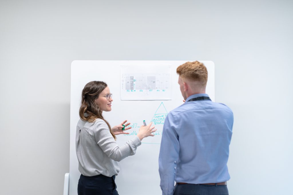 A female and male engineer looking at a white board and collaborating on a project