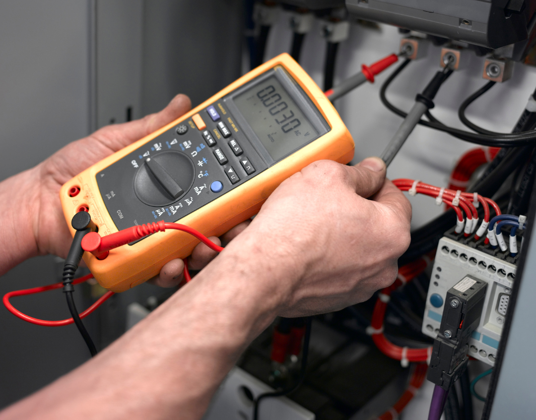 Closeup of person holding a yellow digital multimeter to check voltages of wiring