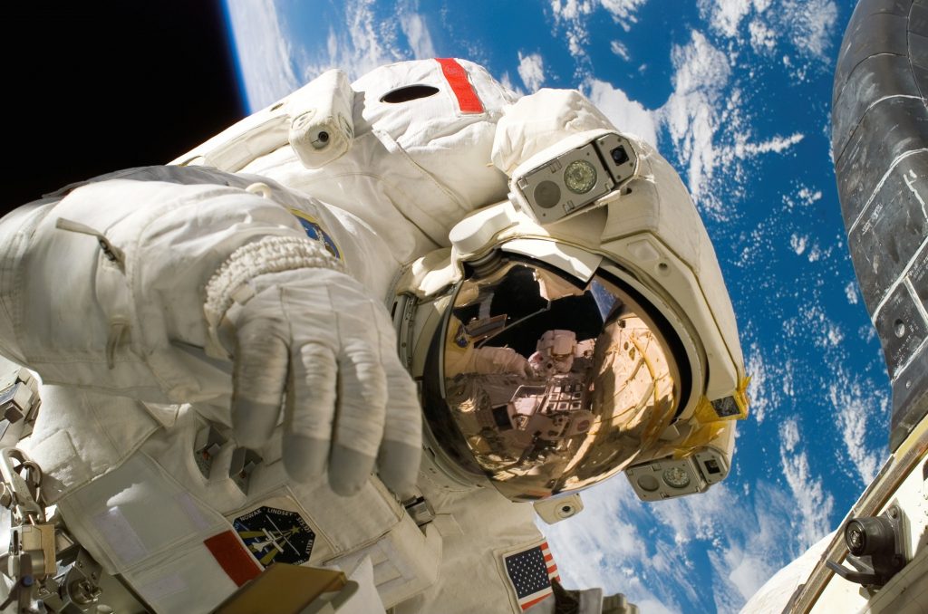 Closeup picture of astronaut in full suit, taking a selfie out in space with earth in the background