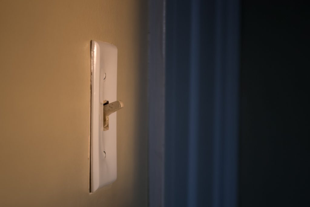 Closeup side angle of white light switch on a tan wall with a blue curtain in the background