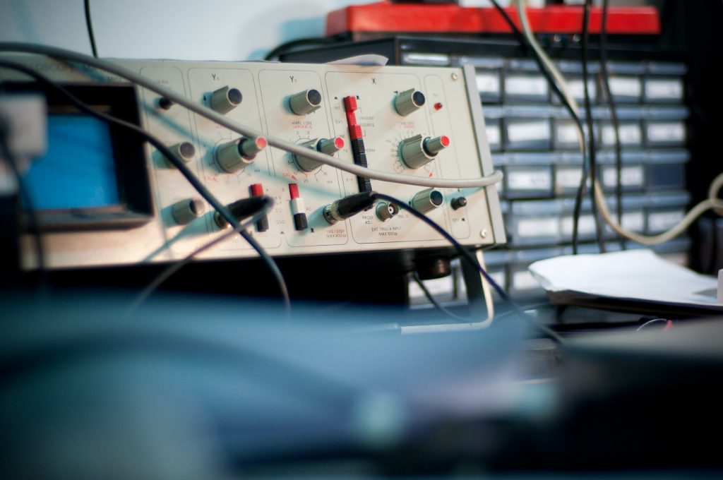 Analog oscilloscope surrounded by cords and lab equipment