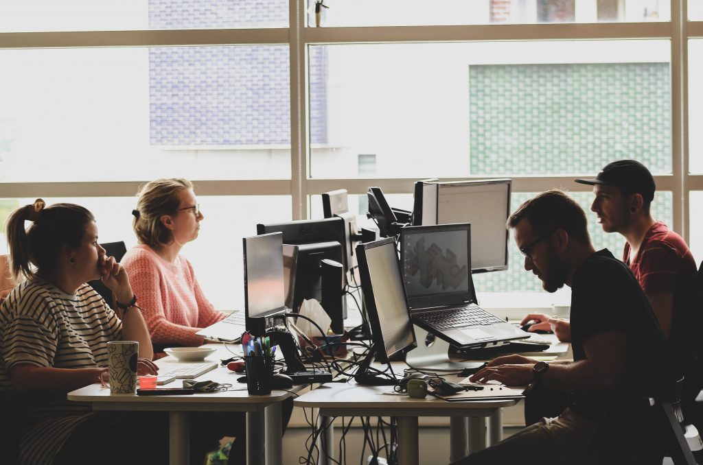 Team of four programmers, 2 women and 2 men, at a large shared desk with multiple computers