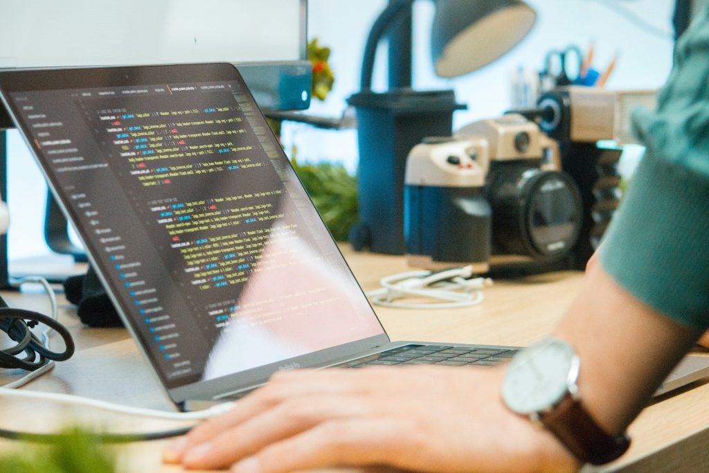 Closeup sideview of a laptop coding in python, with a hand wearing a brown watch in the foreground. 