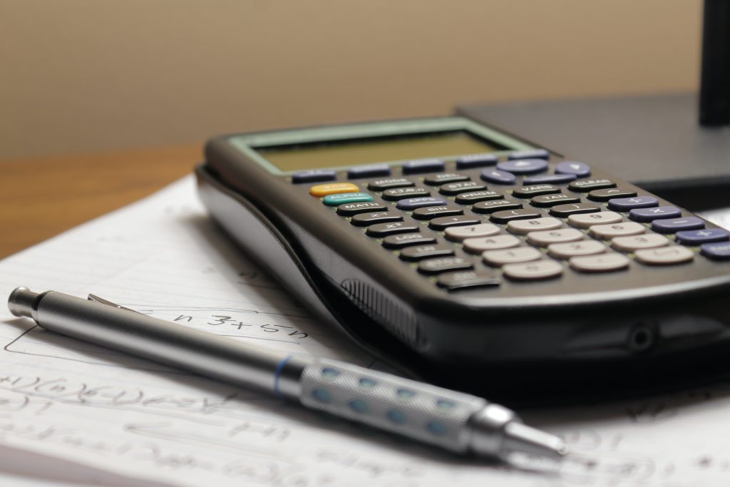 closeup side view of scientific calculator on pad of paper with a pen