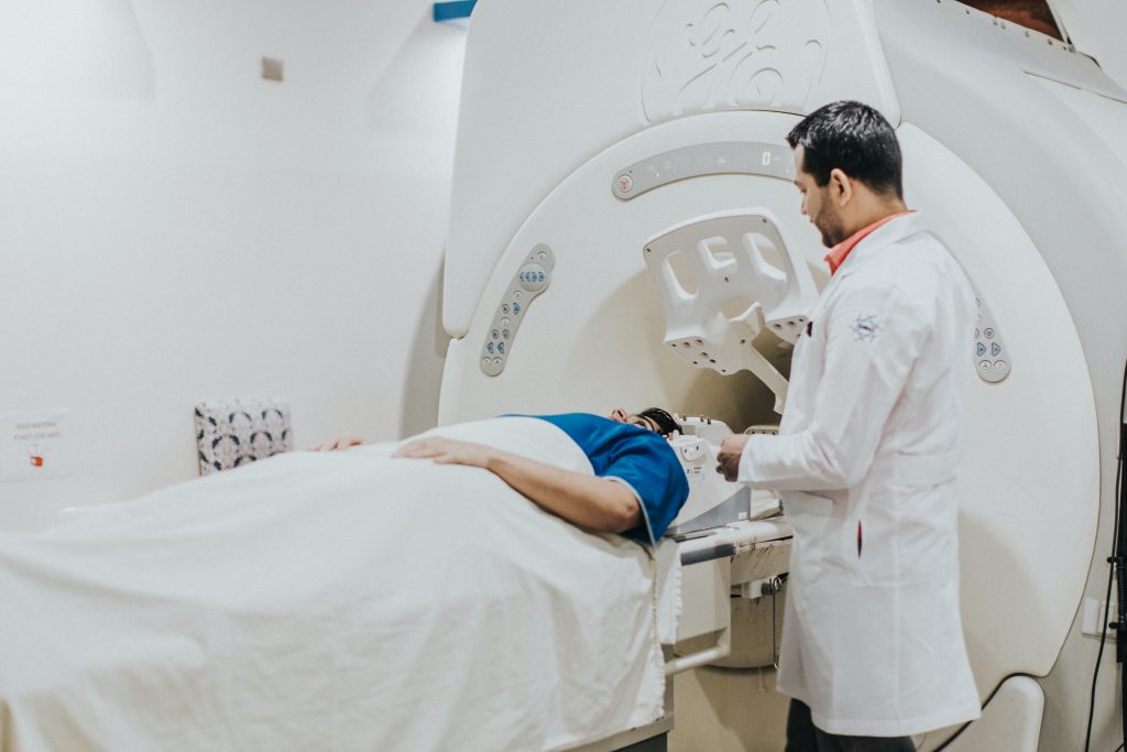 Doctor in white coat talking to patient lying in white MRI machine