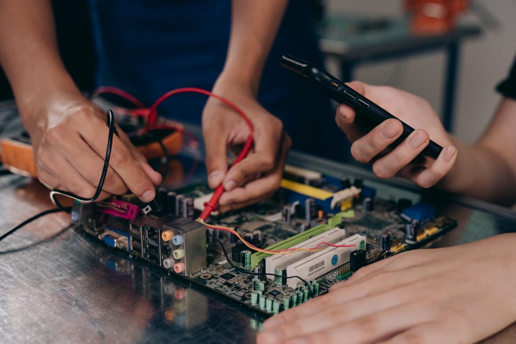 Person testing a circuit board with probes while another person hold a smartphone