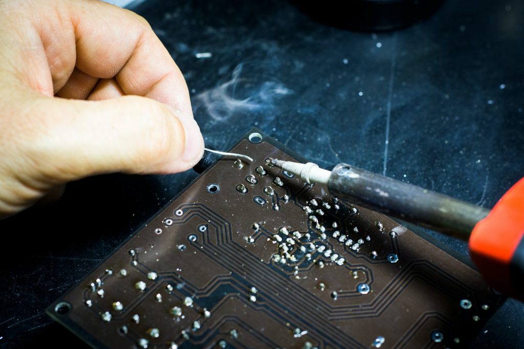 Closeup of person soldering a brown PCB