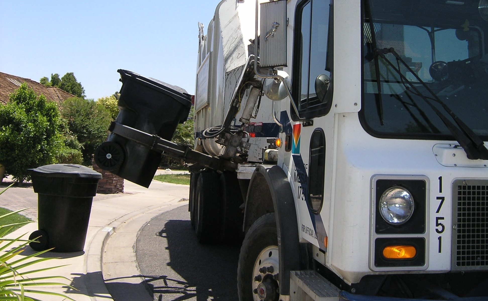 Closeup of white garbage truck collecting trash cans