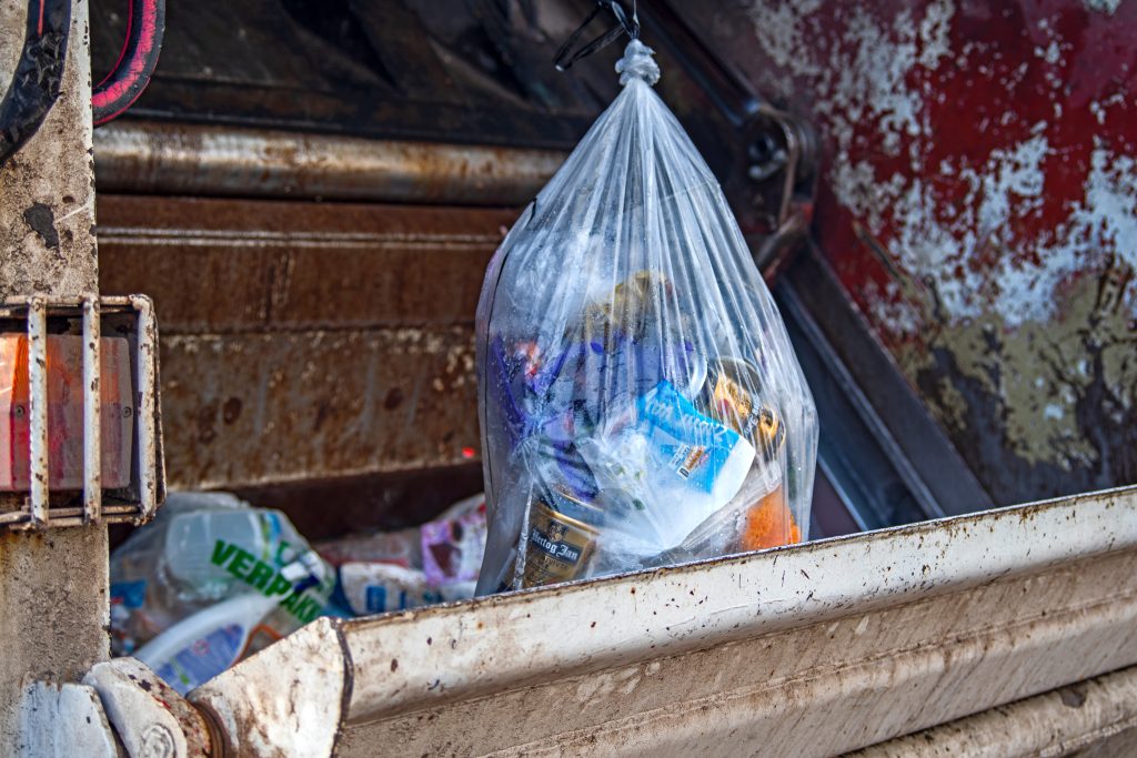 Closeup of clear plastic trash bag full of trash in back of a garbage truck